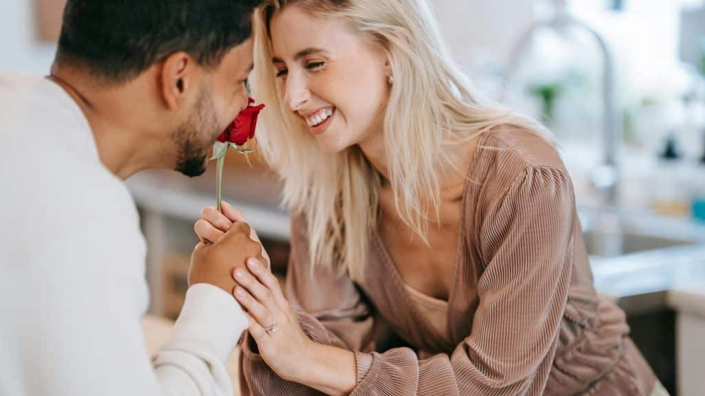 A couple smiling as one smells a red rose held by the other