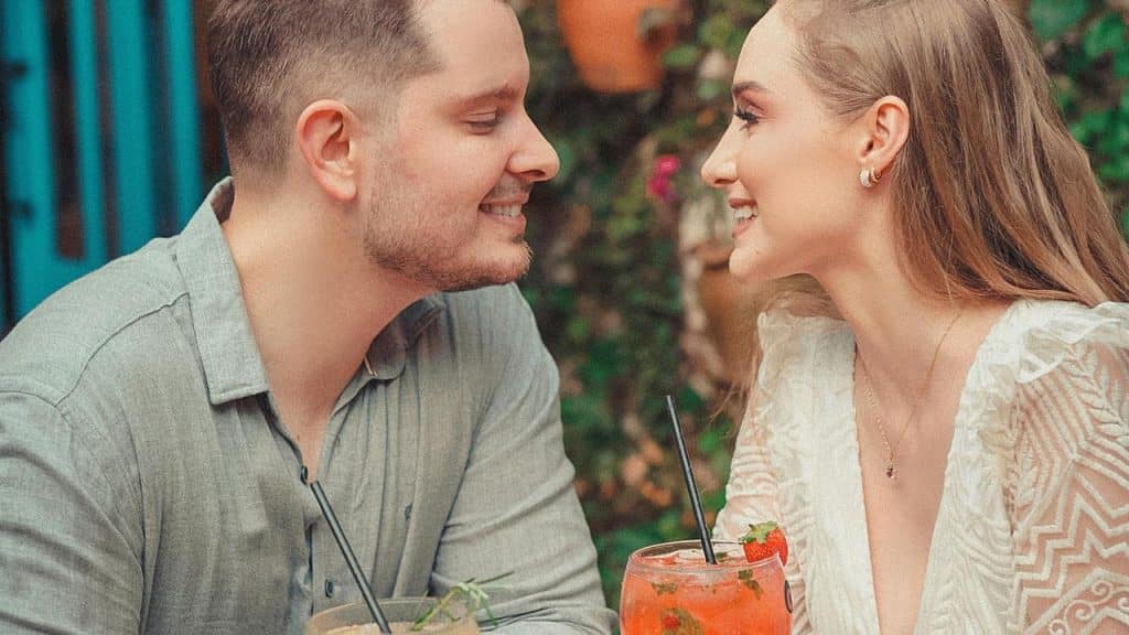A smiling couple facing each other over drinks at an outdoor table
