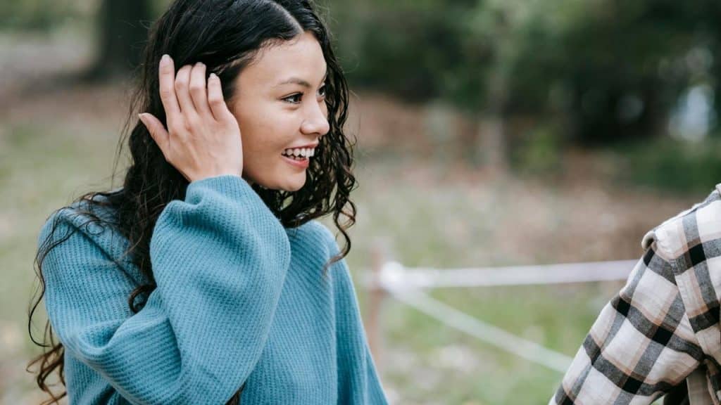 A smiling woman touching her hair while talking outdoors