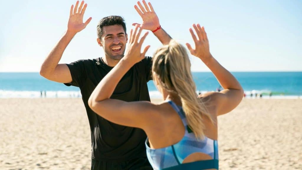 A man and woman high-fiving each other on a sunny beach