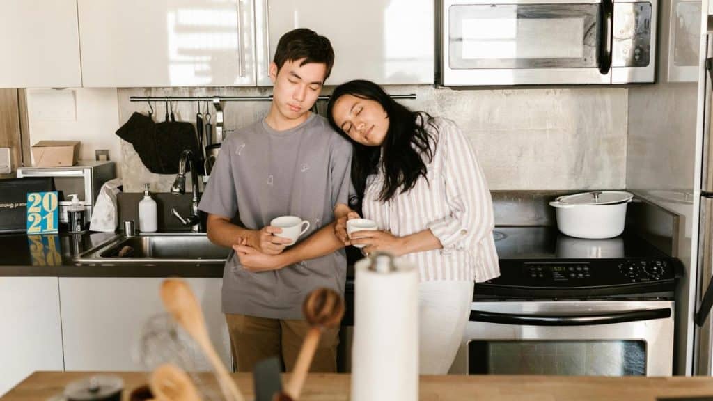A couple resting together in a kitchen while holding mugs