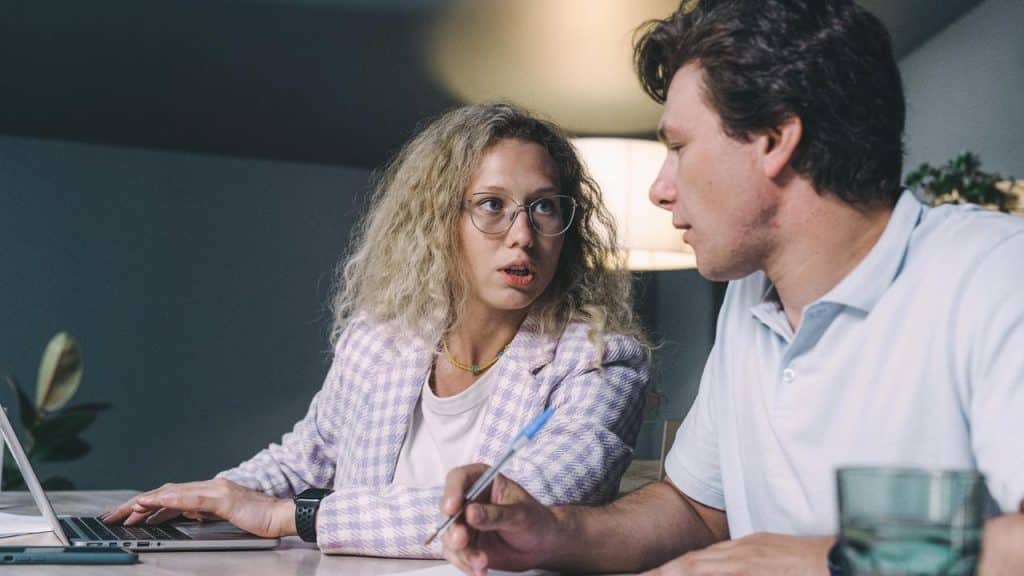 A woman speaking seriously to a man while working together at a table with a laptop.