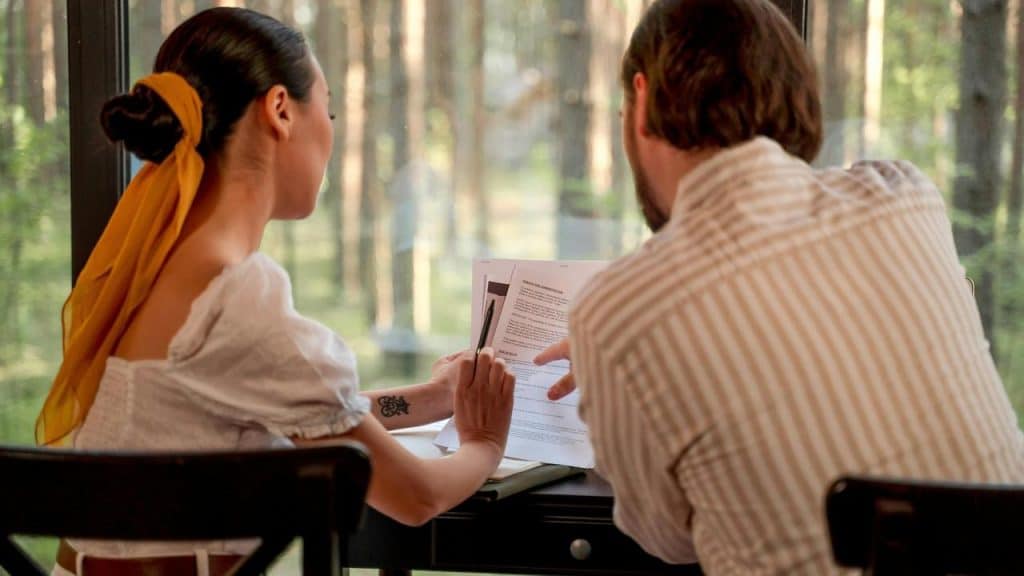 A man and woman reviewing and signing documents together by a window.