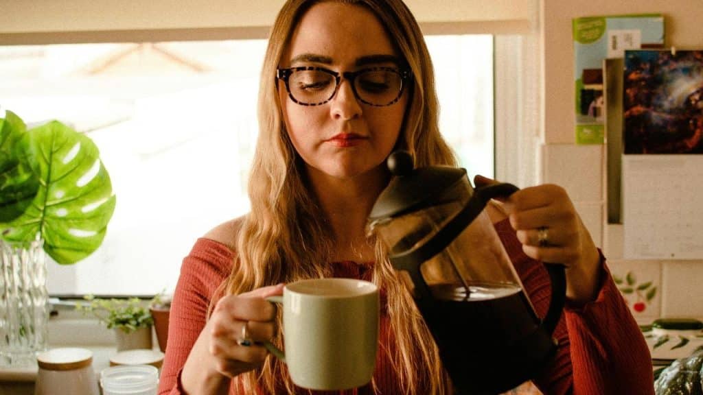 A woman pouring coffee into a mug in a cozy kitchen.