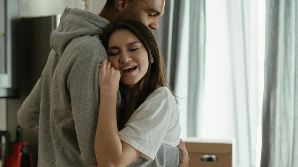A woman smiling while hugging a man in a softly lit room.