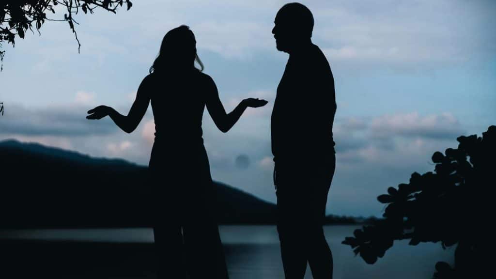 A silhouetted couple standing and talking by the water.
