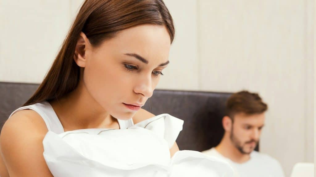 A sad couple sitting on a bed after an argument.