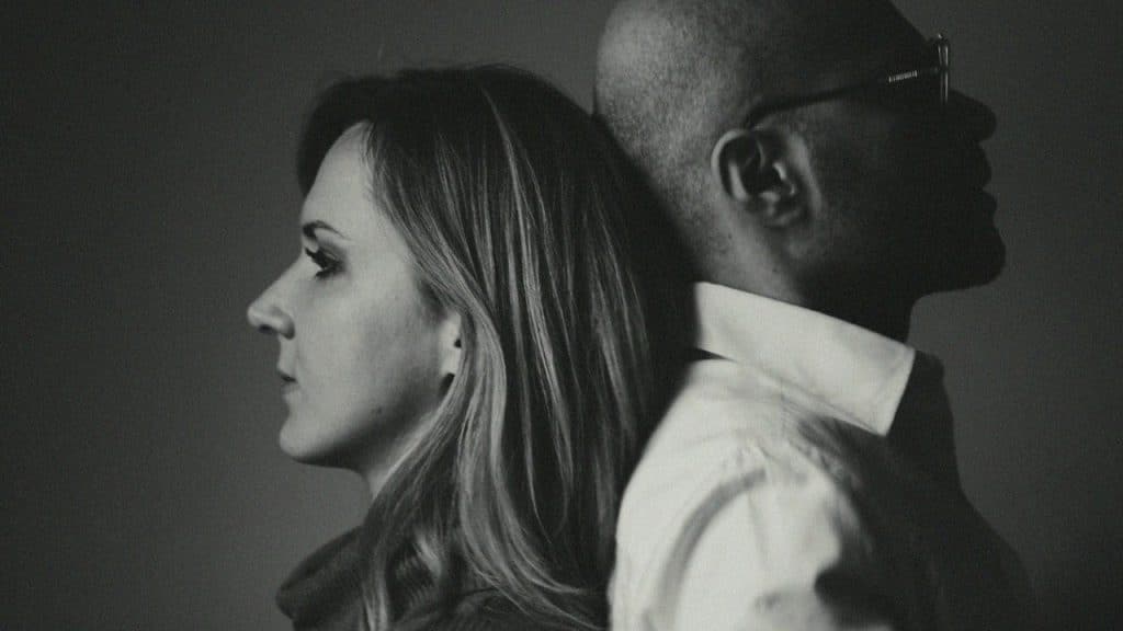 A black and white profile photo of a woman and man leaning back to back.