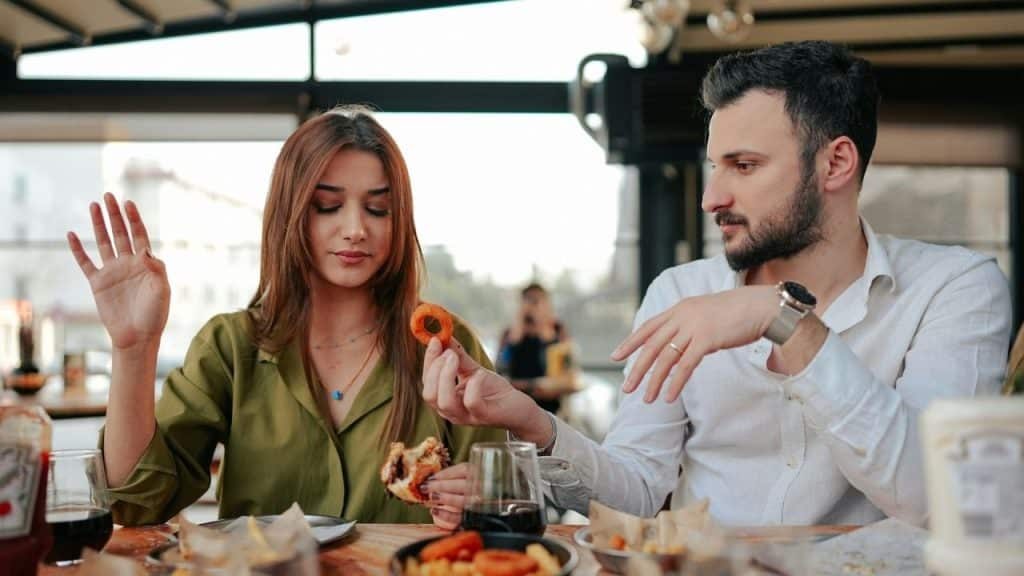 A man offers an onion ring to a woman who is holding up her hand.