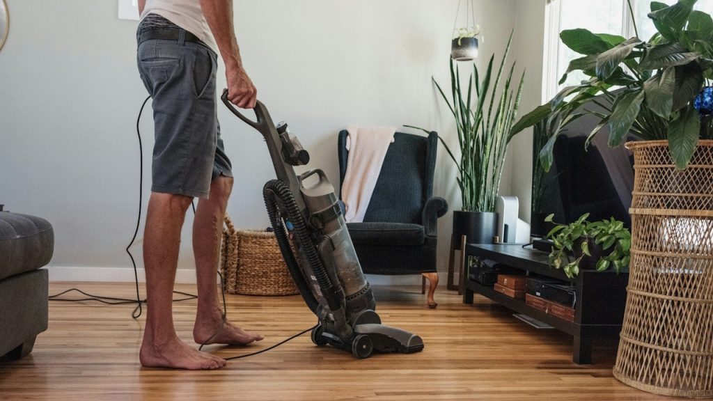 Man vacuuming a hardwood floor in a living room.