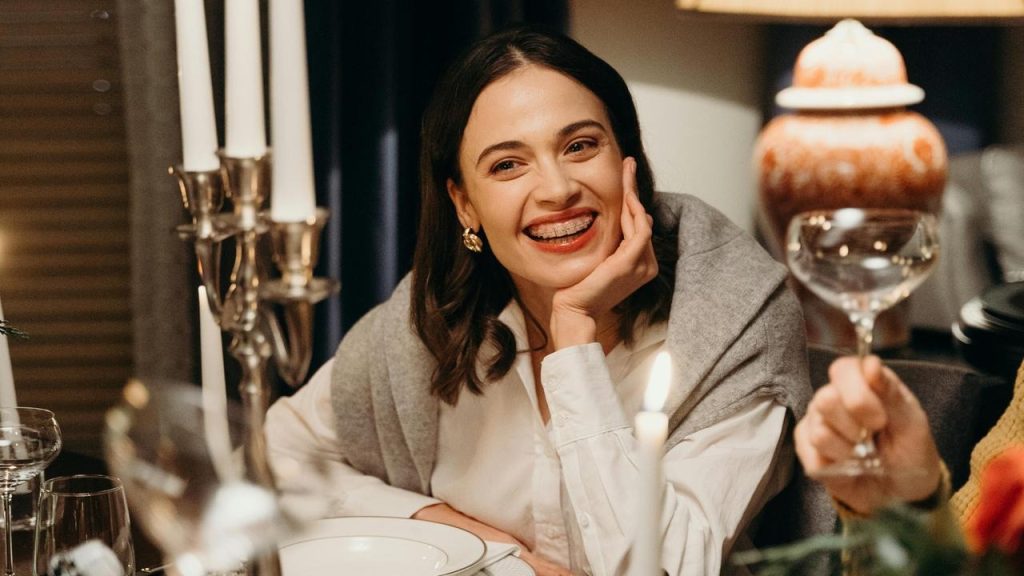 A smiling woman sitting at a candlelit dinner table, resting her chin on her hand.