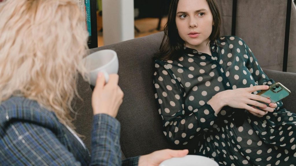 A woman holding a phone while talking to another person sitting beside her on a couch.