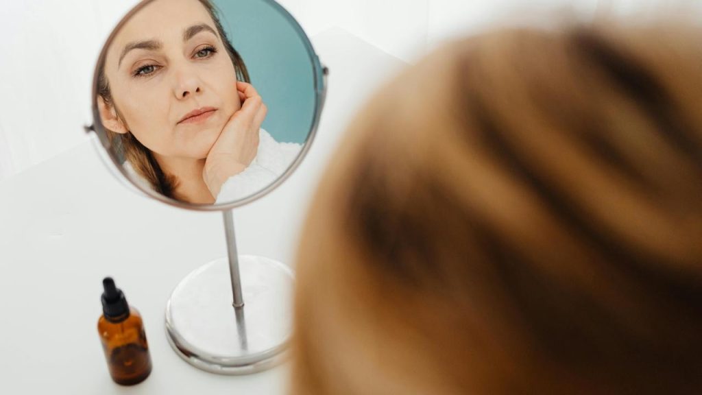 A woman looking at her reflection in a mirror while touching her face.