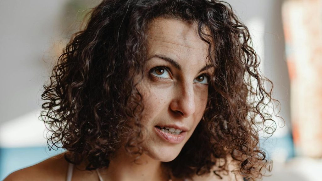 A close-up of a woman with curly hair looking upward thoughtfully.