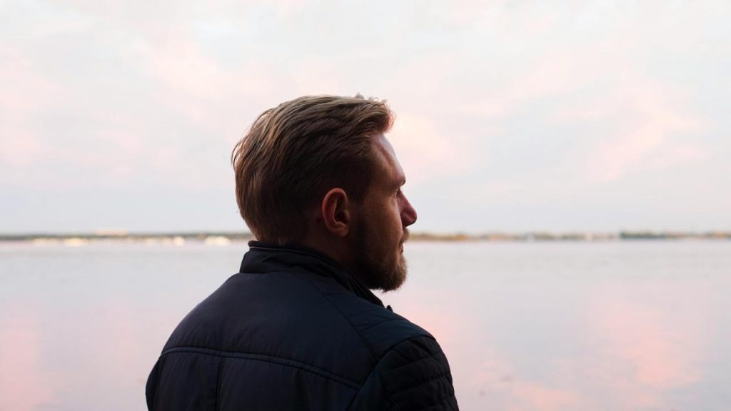 A man looking out over calm water at sunset.