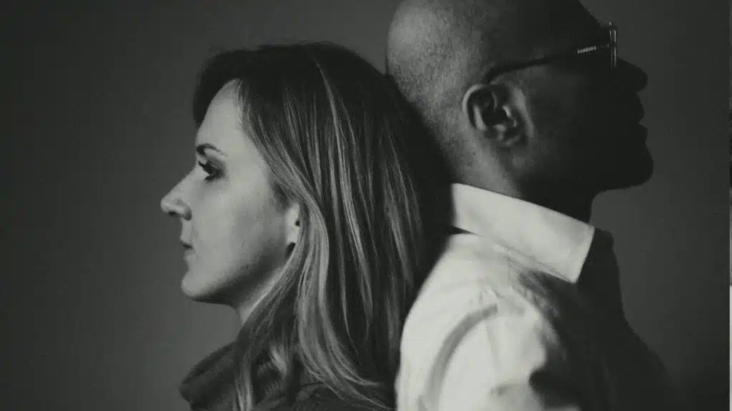 A couple standing with their backs touching each other.