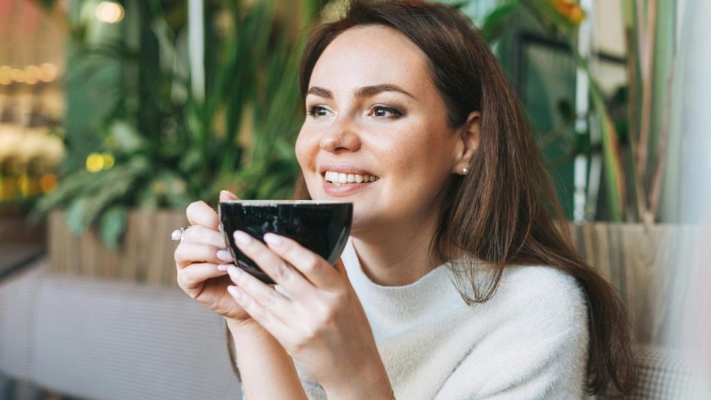 A smiling woman holding a cup of coffee in a bright cafรฉ.