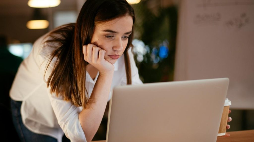 A woman leaning on her hand while looking intently at a laptop.