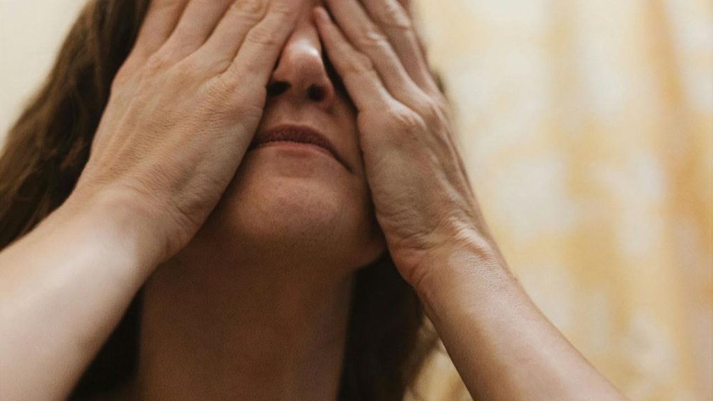 A woman covering her face with both hands in warm light.