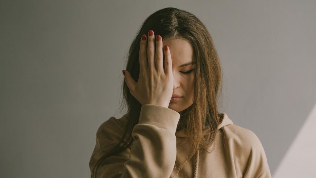 A woman covering one eye with her hand against a plain background.