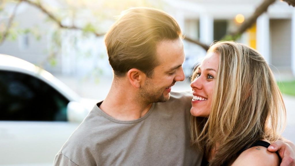 A man and a woman embracing and smiling at each other outdoors in the sunlight.