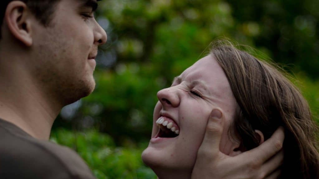 A man’s hands frame the face of a woman who is laughing with her eyes closed.