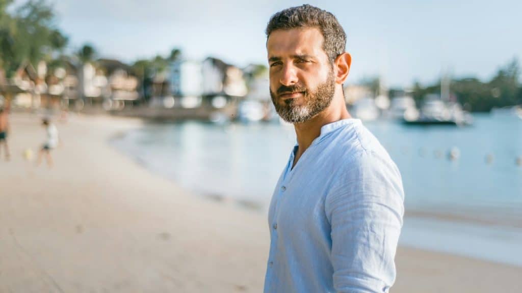 A bearded man standing on the beach.