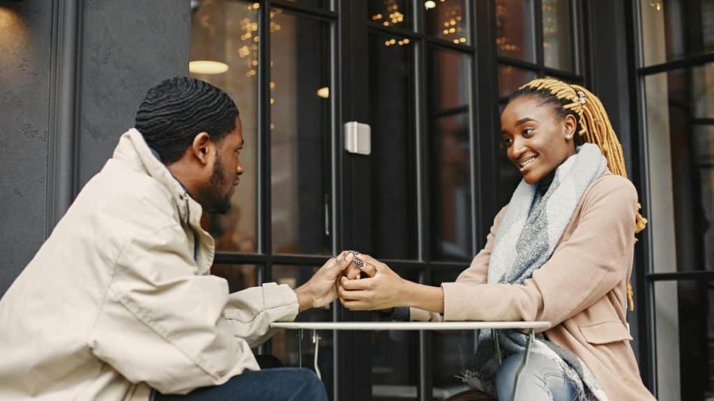 A man giving a ring to a smiling woman while sitting at an outdoor table.
