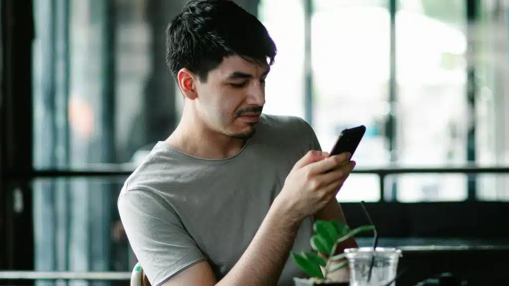 A man sits at a table looking at his smartphone.