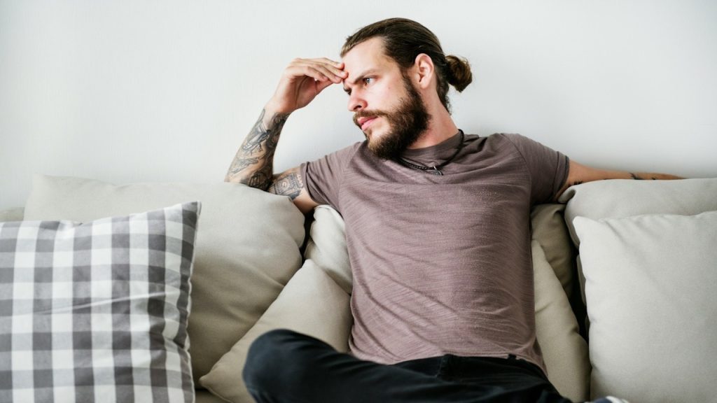 A man with a tattoo is sitting on a couch.