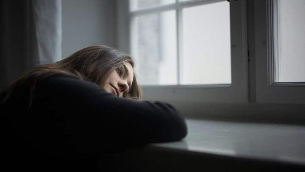 A woman resting her head on a table while looking out a window.