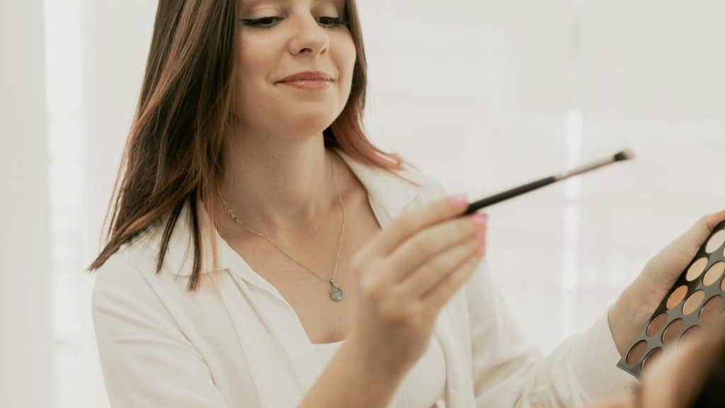 A woman applying makeup with a brush and palette.
