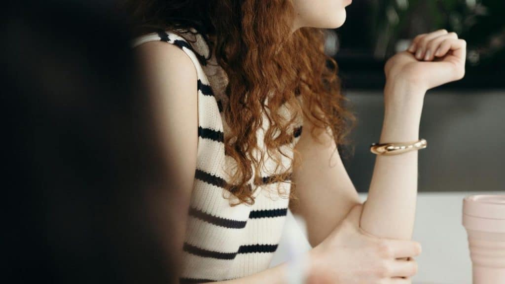 A person with curly hair wearing a striped sleeveless top sitting at a table.