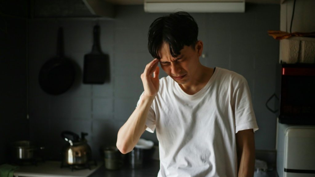 A man feeling a headache while he is standing in a kitchen.