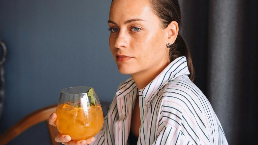 A woman holding an orange drink and looking thoughtfully to the side.