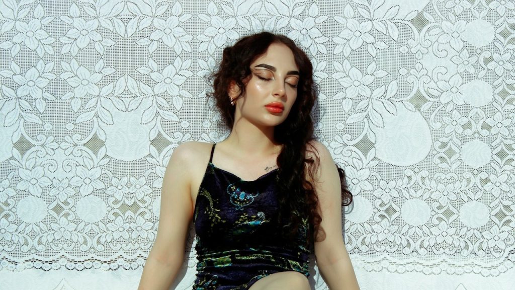 A woman wearing a black dress sitting on the floor with her legs crossed.
