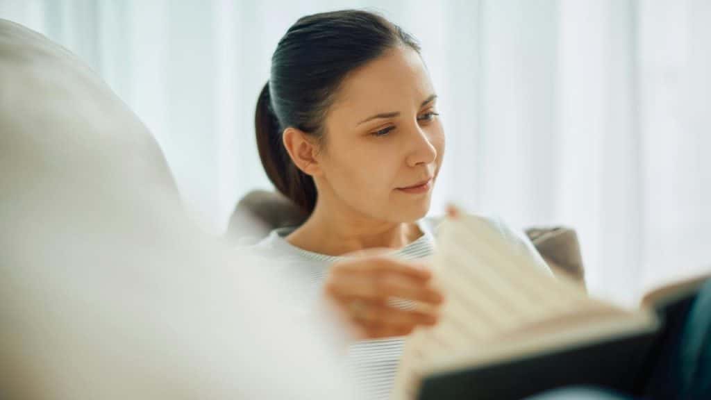 A woman reading a book while sitting comfortably indoors.