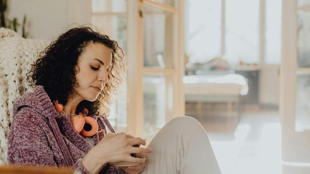 A woman sitting at home using her phone with headphones
