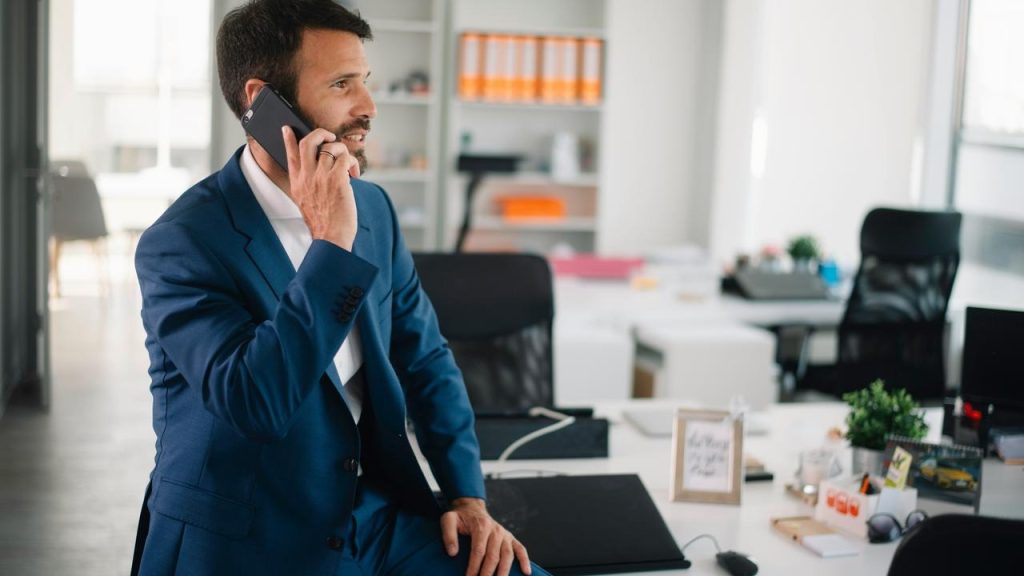 A man in a suit talking on a phone in a modern office.