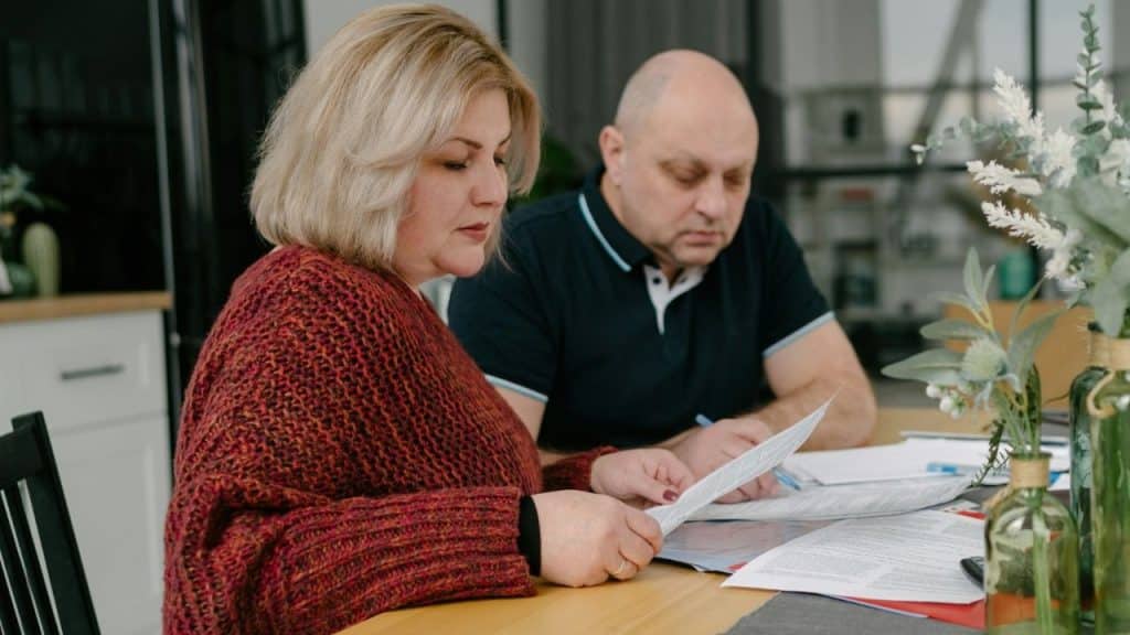 A woman and a man sit at a table reviewing several pieces of paper together.
