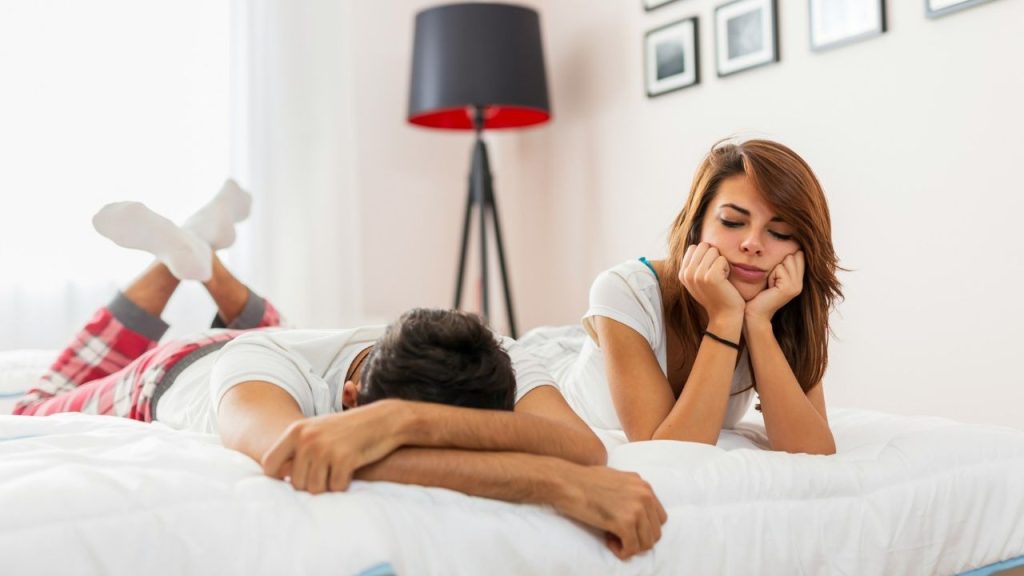 A woman rests her chin on her hands while a man lies face down beside her.