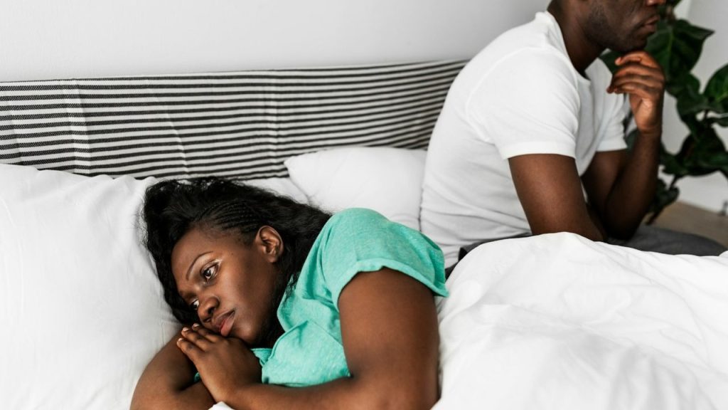 A woman in a green shirt lies in bed, looking away from a man.