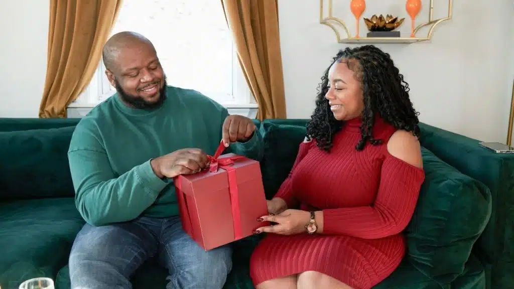 A man in a green shirt unties a red gift box held by a woman in a red dress.