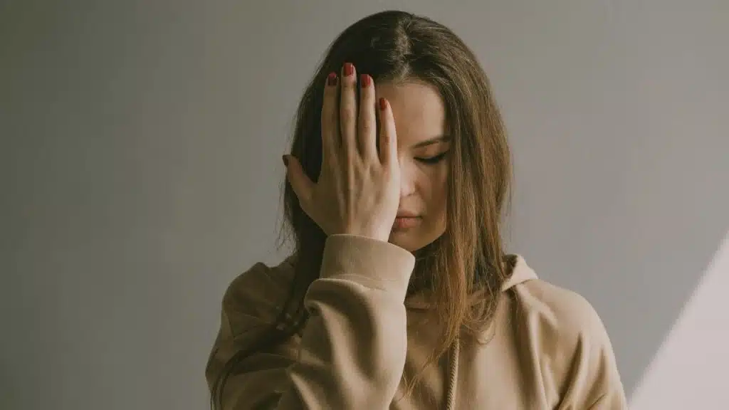 A woman with red-painted nails is covering her face with one hand.