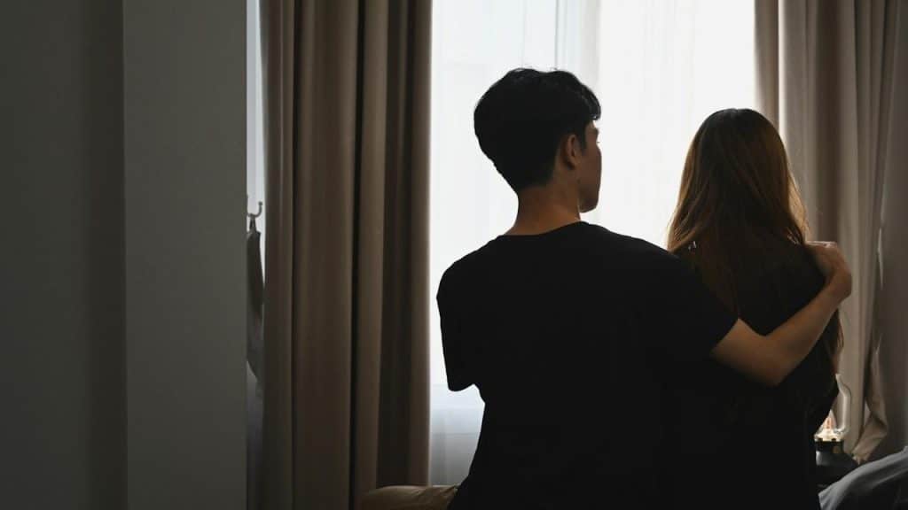 A young man is embracing his girlfriend and sitting in the bedroom.