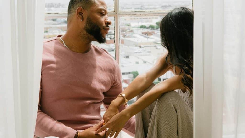 A man and a woman are sitting on a windowsill.