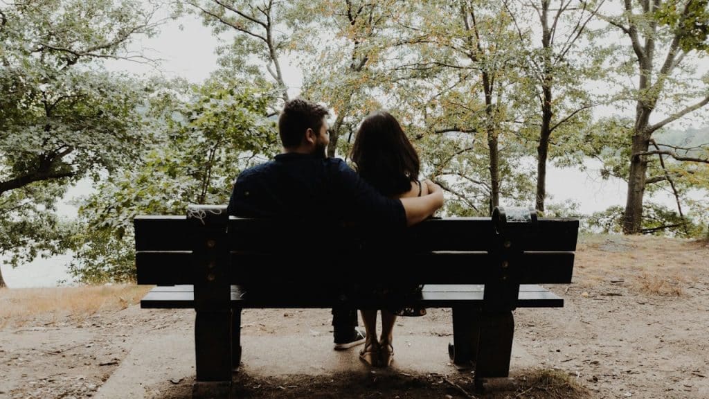 A couple sitting on a bench overlooking a body of water and talking.