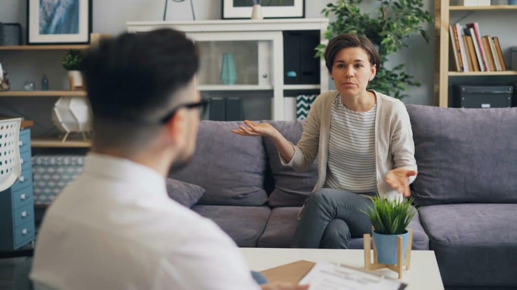 A woman arguing with a man as she sits on a couch.